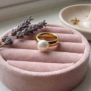 Macro view of large white pearl on wide gold stainless steel band in jewelry tray