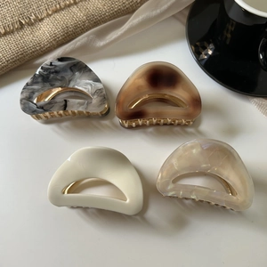 Detail of four acetate hair claws in marble and tortoiseshell patterns on silk fabric