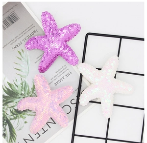 Detail of glitter starfish hair clips in purple, pink, and white on a tropical background