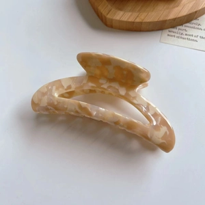 Detail view of large acetate hair claw clip with beige amber pattern in moon shape