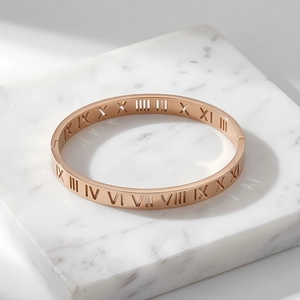 Detail of rose gold bangle with hollow roman numeral engravings on marble surface