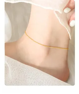 Close-up of minimalist gold snake chain anklet worn on ankle against white fabric background