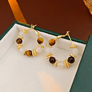 Detail of gold-plated hoop earrings with tiger eye stones in a green jewelry box