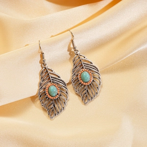 Detailed view of bohemian leaf earrings with turquoise stones on gold silk background