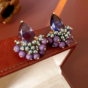 Macro detail of teardrop purple crystal and beaded earrings on a vintage jewelry box