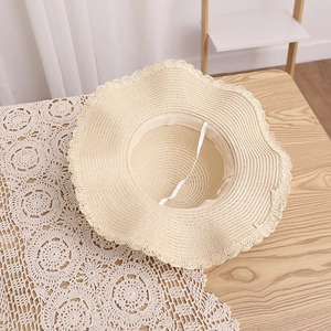 Detailed texture of off-white woven straw sun hat with scalloped edge and wind rope