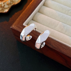 Macro shot of silver irregular geometric C-shaped hoop earrings on a wooden box