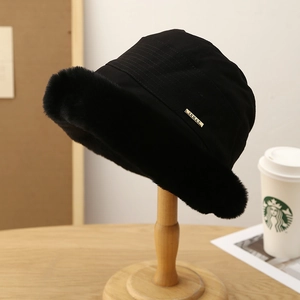 Detail of plush black bucket hat with faux fur brim and a gold ISHAT metal logo