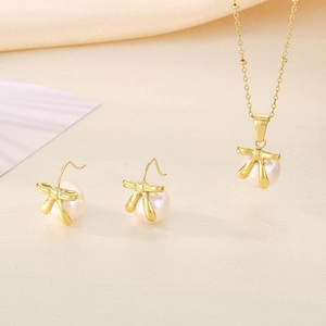 Detail of gold bow earrings and necklace set with white pearls on warm background