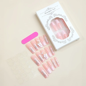 Detail of pink French press-on nails with 3D bows, pearls, and application tool kit
