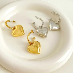 Polished gold and silver 3D heart drop earrings in a white ceramic tray display