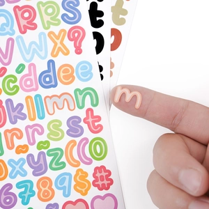 Macro detail of 5mm colorful alphabet stickers being held to show small scale for scrapbooking