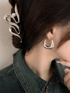 Gros plan de boucles d'oreilles argentées en U et d'une barrette à perle portée par un modèle
