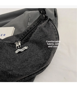 Close-up of crescent denim shoulder bag featuring a white woven label and silver zippers
