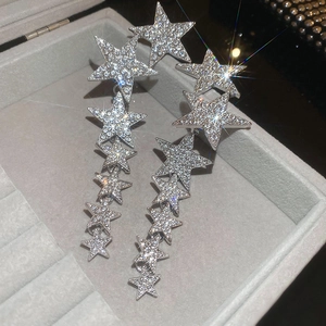 Detailed view of silver star tassel earrings with sparkling crystals on grey velvet