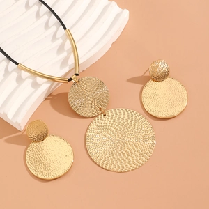 Close-up of golden geometric round necklace and earrings with hammered texture