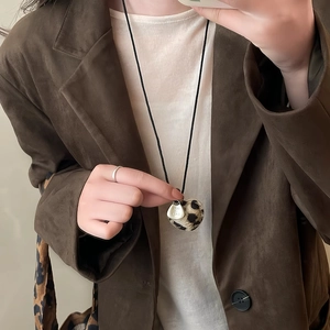 Close-up of leopard print heart pendant with metal tag on a braided necklace