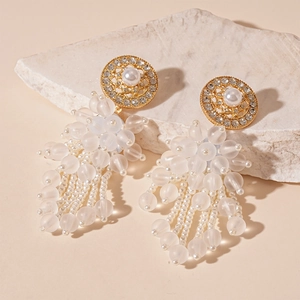Vue macro de boucles d'oreilles dorées avec perles blanches et pompons en perles dépolies