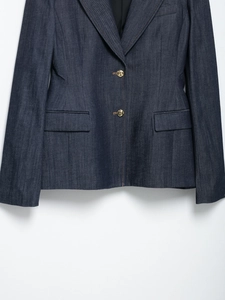 Dettaglio frontale di un blazer in denim blu scuro con cuciture arancioni e bottoni dorati