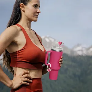 Pink 40oz insulated tumbler with heart straw cover and decorative chain in nature setting