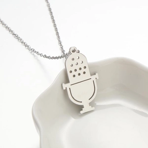 Collier avec pendentif microphone en acier argenté sur une assiette en céramique blanche