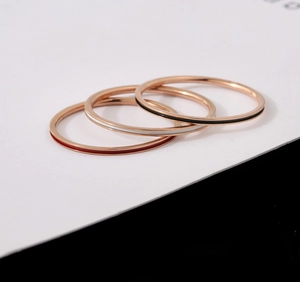 Close-up of three minimalist rose gold stackable rings with red, white and black enamel bands
