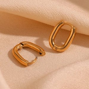 Macro shot of gold plated oval geometric earrings on beige pleated satin fabric