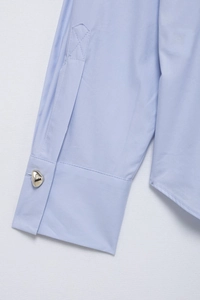 Detail of light blue striped shirt cuff featuring a unique silver irregular metal button