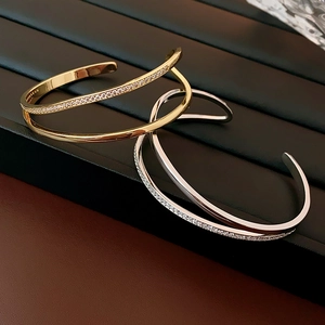 Detail of gold and silver open bangles featuring layered zircon stones on a dark tray