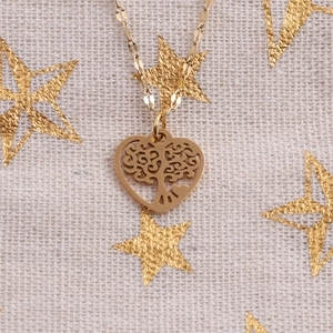 Detailed view of a gold heart pendant featuring a tree of life cutout on beige fabric