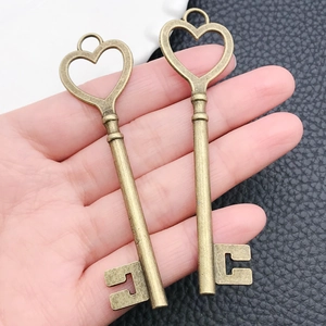 Close-up of hand holding two vintage heart-shaped bronze metal skeleton key pendants
