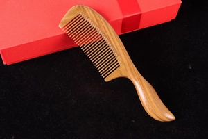 Detailed view of a green sandalwood comb next to a red gift box on a black background