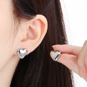 Detailed view of silver heart-shaped stud earrings worn and held for scale and finish