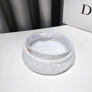 Detail of white lace beret with M logo charm and breathable mesh fabric texture