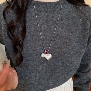 Detail of silver bead chain necklace with white matte heart and ball pendants on a sweater