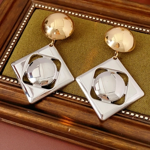Macro shot of two-tone gold and silver geometric earrings on a vintage wooden frame