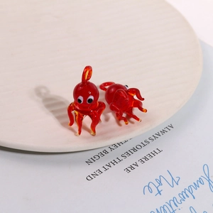 Macro detail of two translucent red glass octopus charms on a white ceramic plate