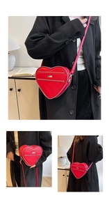 Detail of red heart-shaped leather crossbody bag featuring stylish silver metal zippers