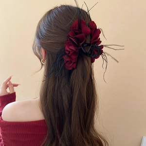 Detail of burgundy floral hair claw with feathers worn on model's brown hair