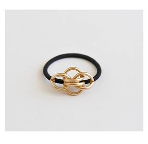 Close-up of golden metal knot buckle on a black elastic hair tie against a white background
