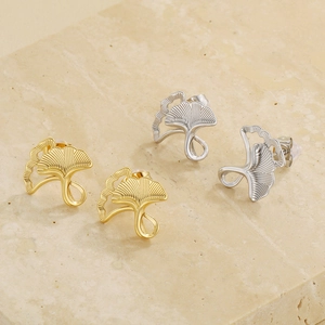 Detailed view of ginkgo leaf stud earrings in gold and silver on marble background