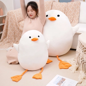 Cute white plush duck dolls in two sizes displayed in a cozy bedroom setting