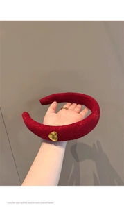 Macro view of a thick dark red fabric headband featuring a gold heart-shaped metal charm