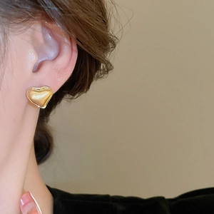 Close-up of golden heart earrings with matte brushed texture and polished edges on ear