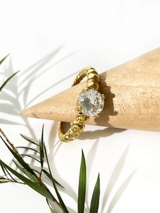 Macro shot of 18K gold ring with round zircon on a wooden stand with natural shadows