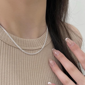 Close-up of a delicate silver chain necklace worn by a model against a beige sweater