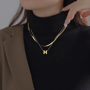 Detail of layered gold snake chain necklace with an H pendant on a female model