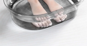 Close-up of a clear plastic foot soak basin with warm water and submerged feet