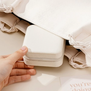 Portable beige leather jewelry box being placed into a bag for travel storage