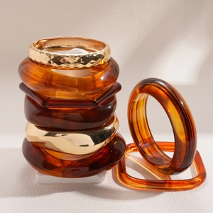 Set aus retro bernsteinfarbenen Acryl- und goldfarbenen Metallarmbändern auf weißem Sockel